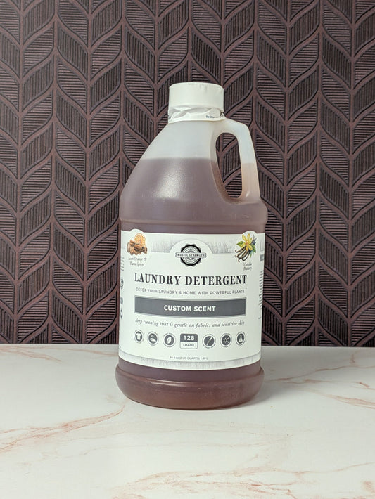 Rustic Strength, Laundry Detergent, Half Gallon, Plastic Jug, Sweet Orange & Warm Spices & Vanilla Buttery set on a light marbled surface with a patterned backdrop