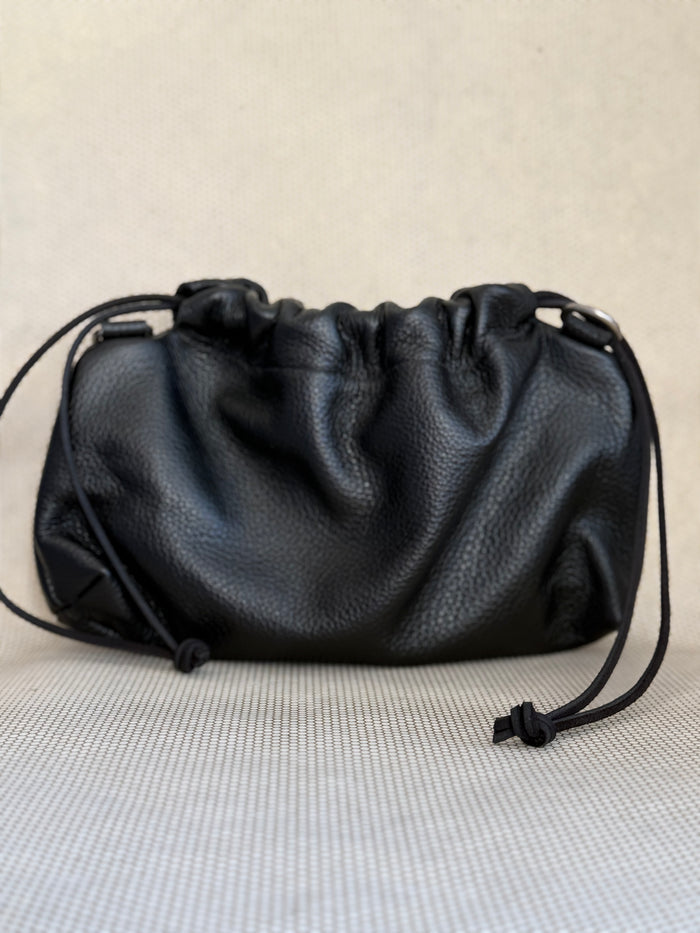 Black leather pouch bag with drawstring and strap on a light gray background.