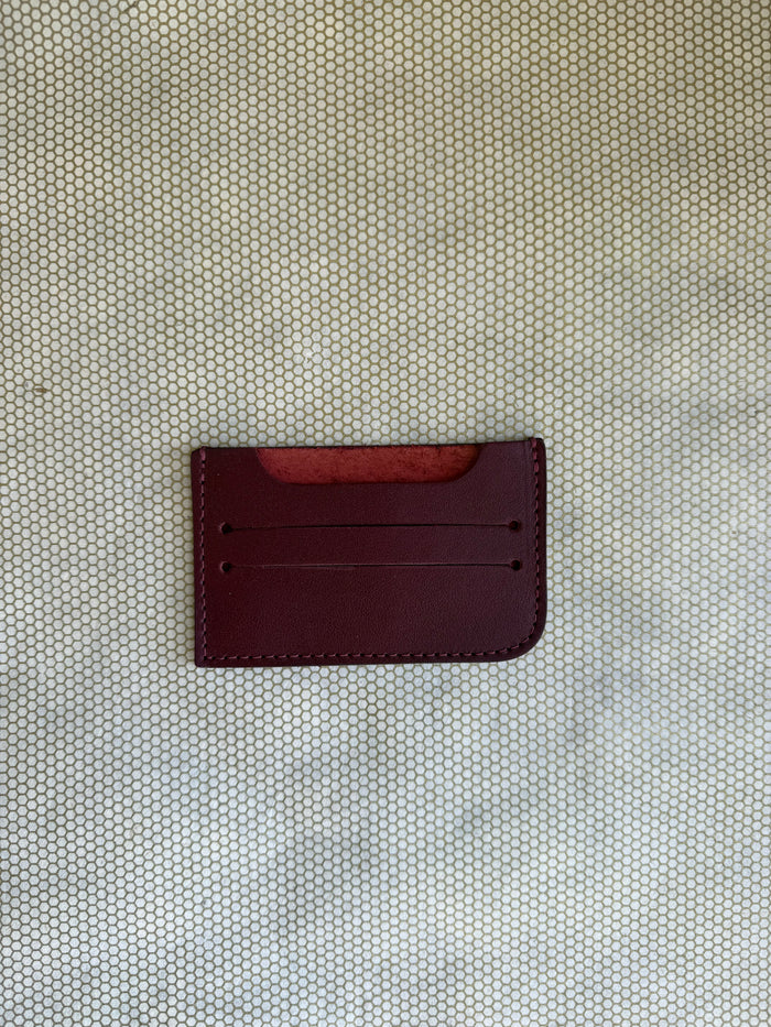 Maroon leather cardholder on a textured beige surface