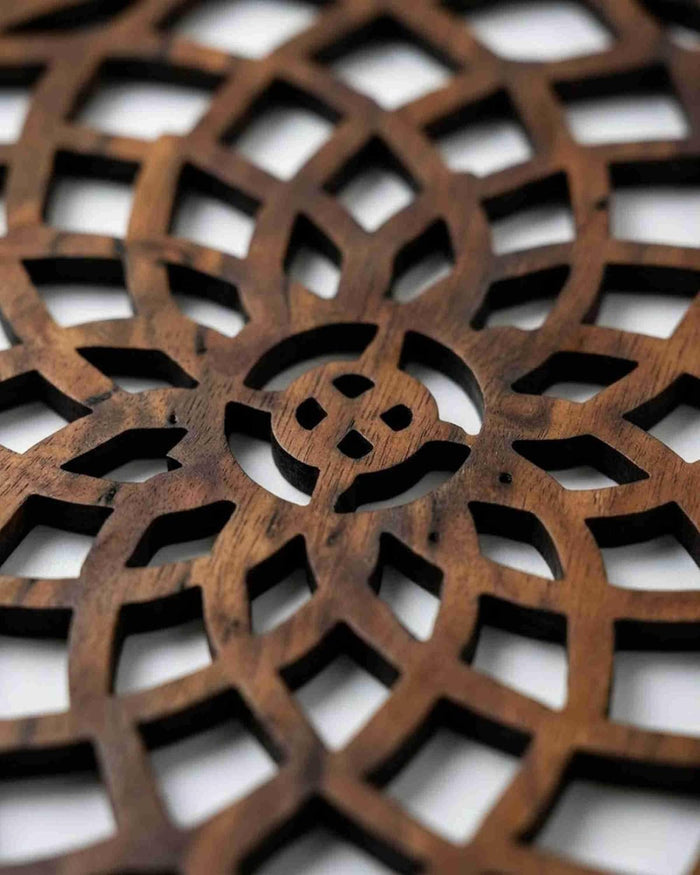 Light brown round wooden trivet with spiral floral lattice cutout pattern