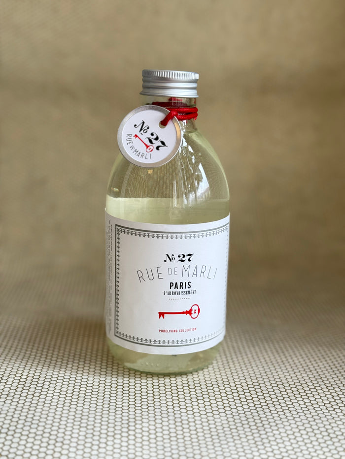 glass bottle of rue de marli foaming bath with white label on neutral background.